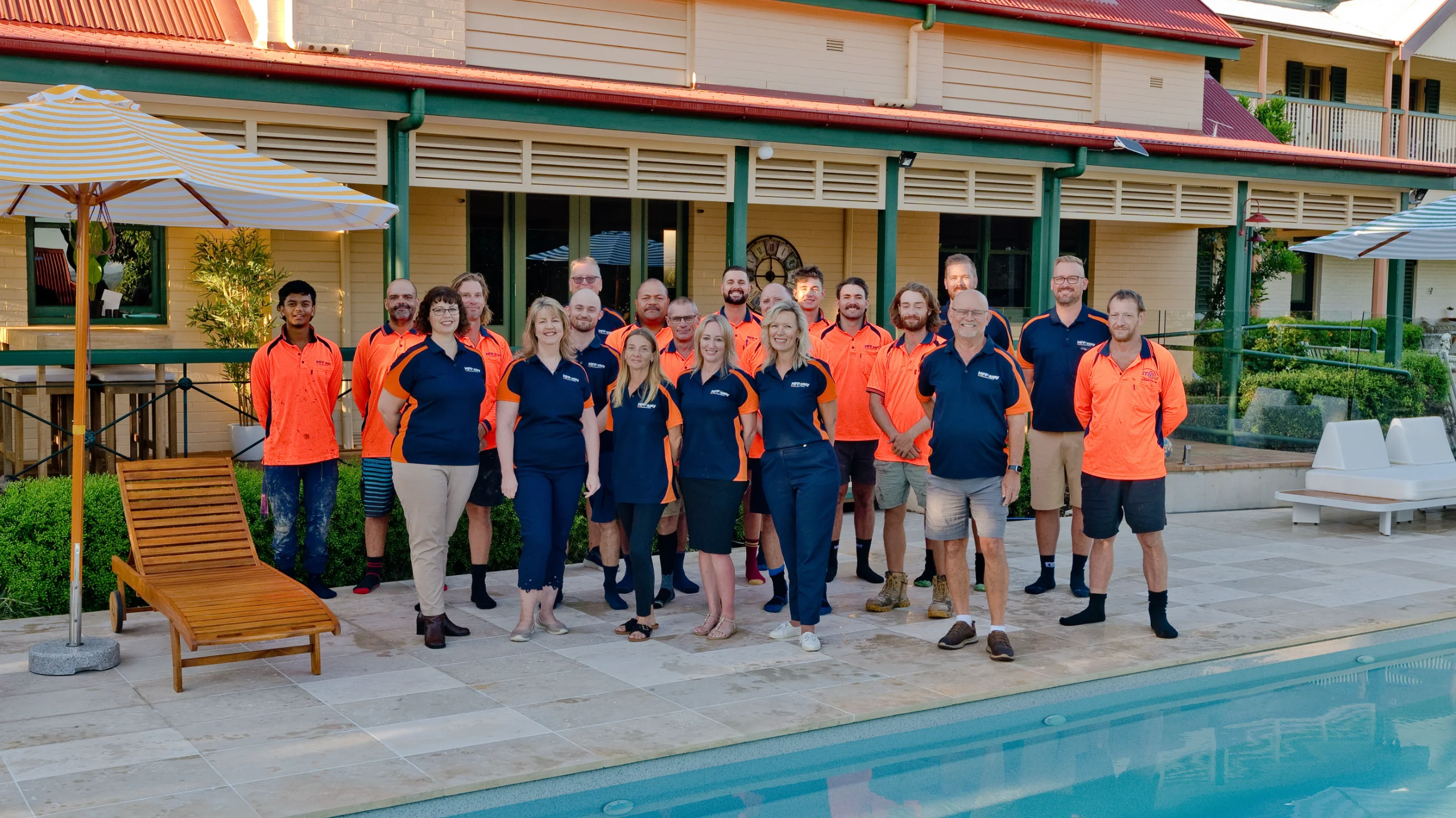 The MFP Easy team in branded orange and navy uniforms gathered poolside beside a Queenslander-style house