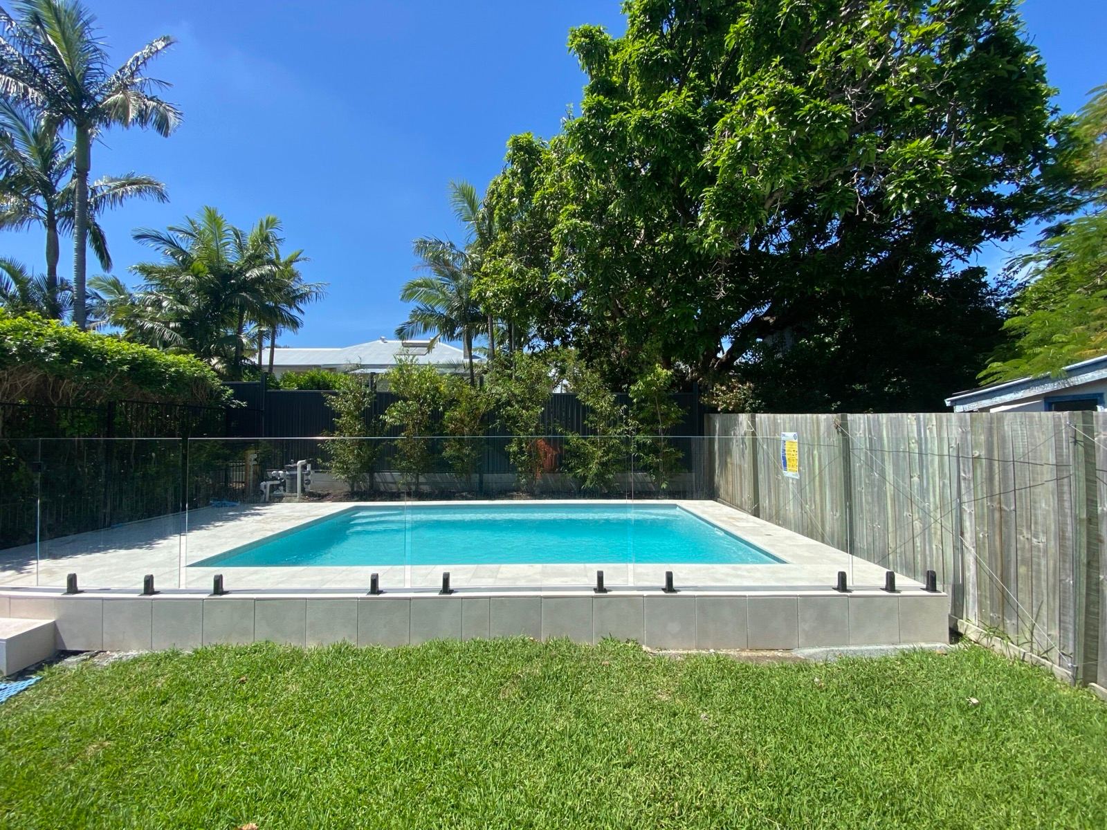 Frameless glass pool fence around a rectangular pool bordered by stone pavers and timber fencing