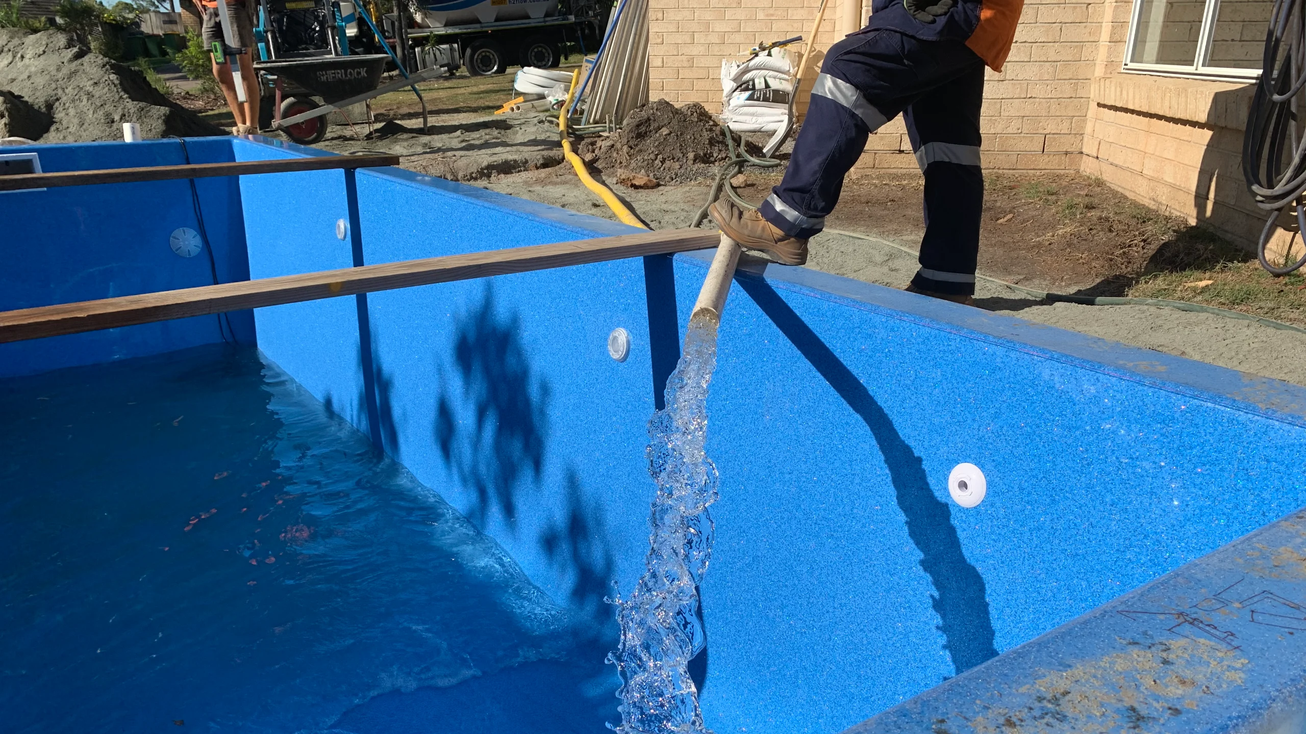 An MFP Easy installer fills a new blue fibreglass pool shell with a hose during a backyard install in progress