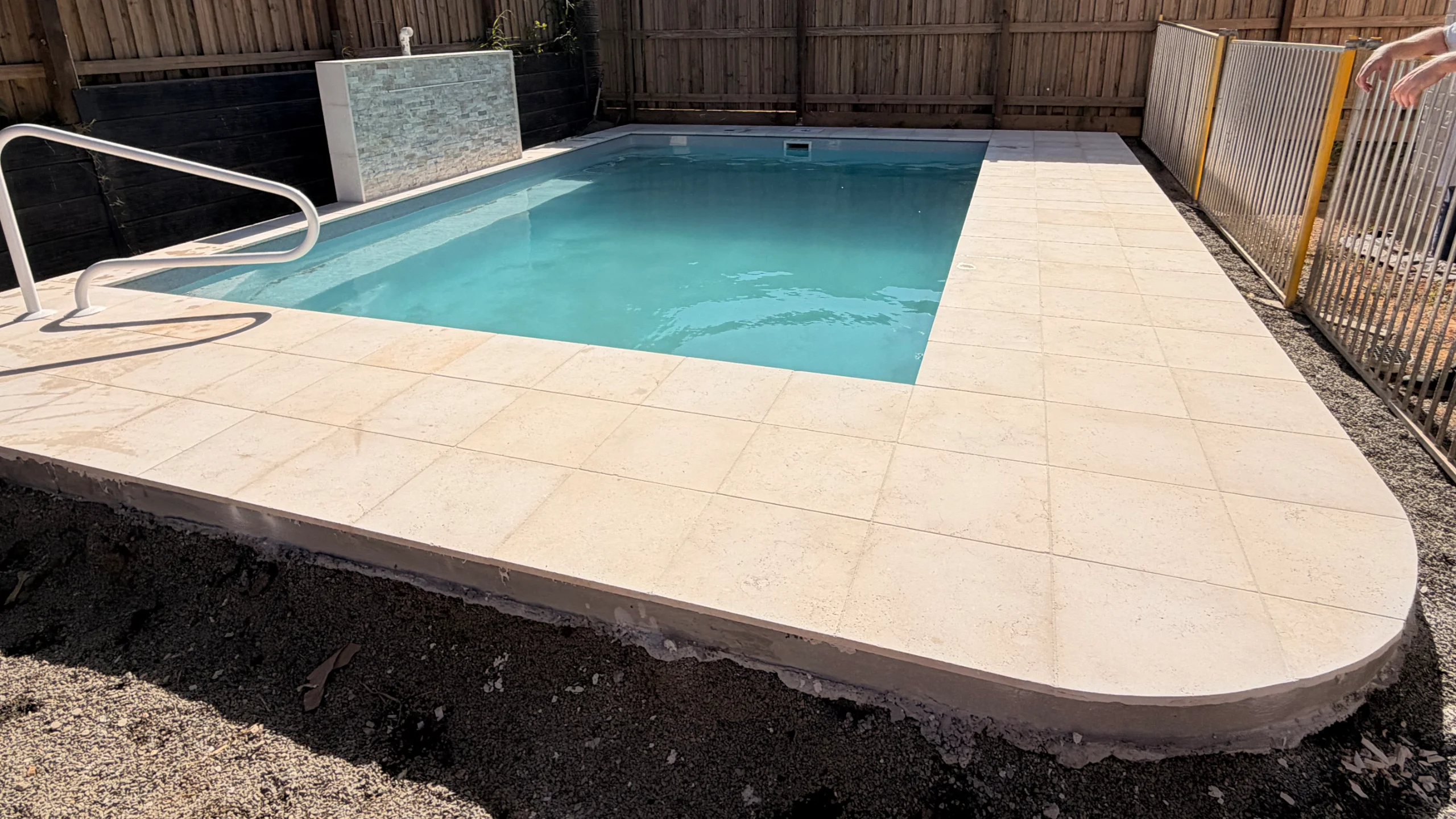 Freshly laid large-format cream stone paving and curved coping around a fibreglass pool, landscaping still in progress