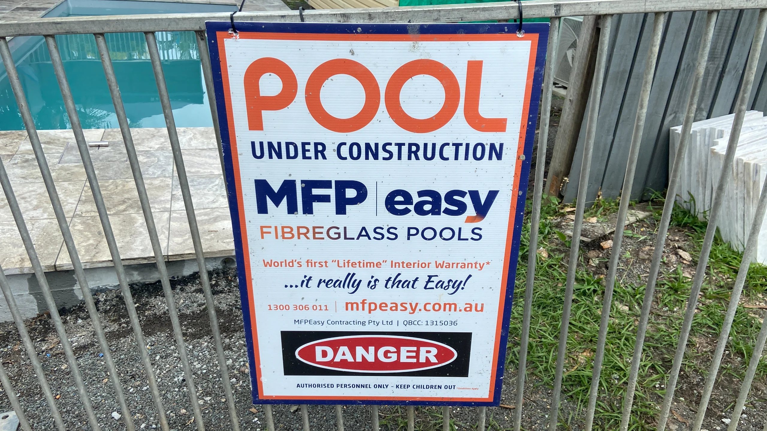 Metal pool safety fence with a Danger warning sign during MFP Easy fibreglass pool construction