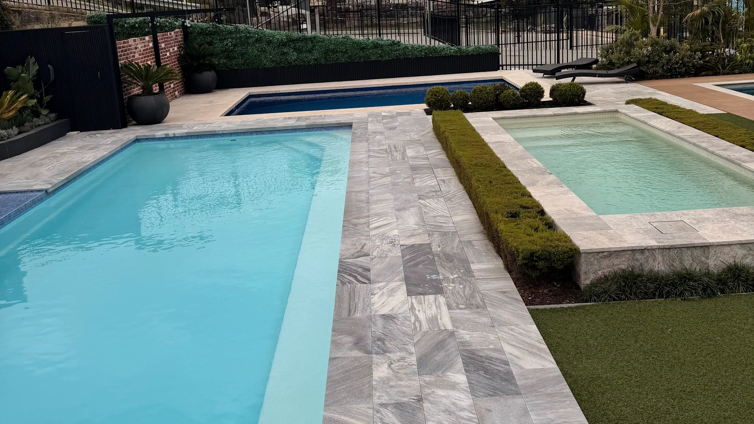 Multiple rectangular fibreglass pools in a display centre with grey stone paving and clipped hedges