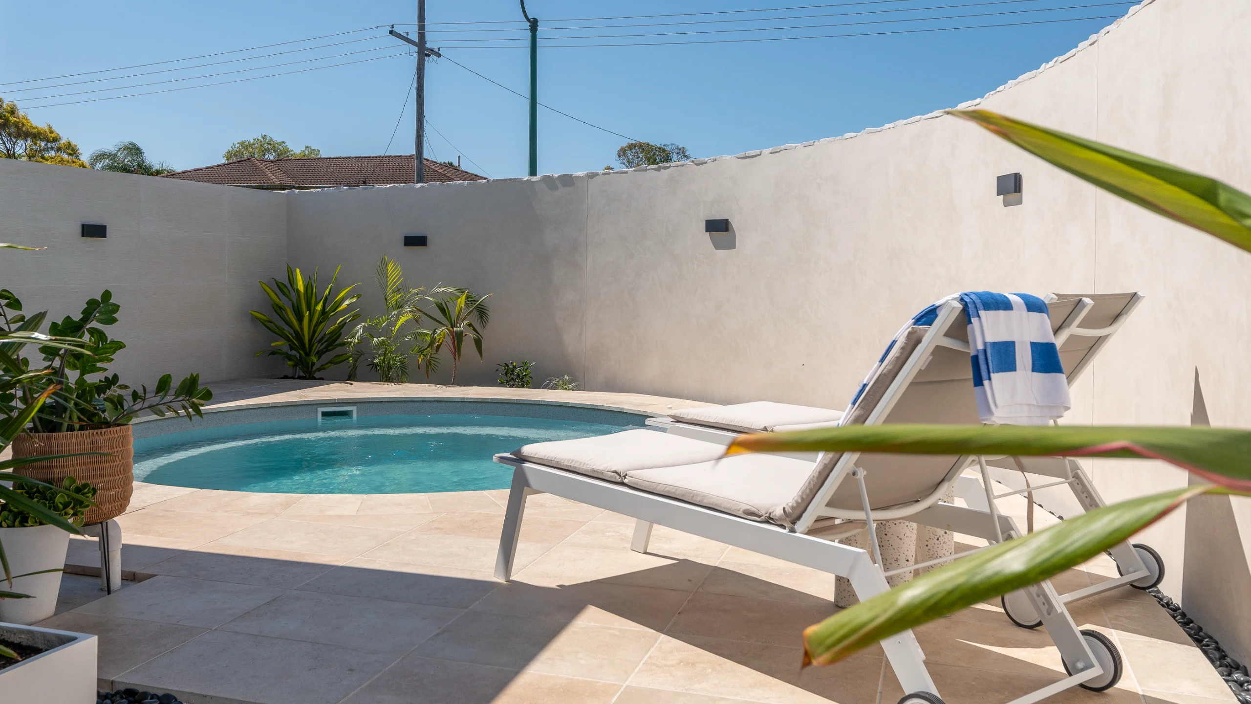 Round fibreglass pool set in cream stone paving with sun loungers and a rendered courtyard wall