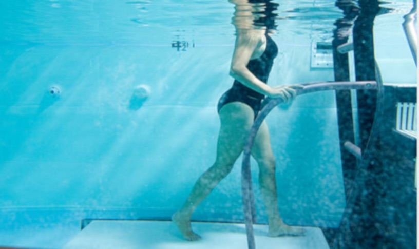 Underwater view of a person running along the floor of a therapy pool while gripping a submerged handrail